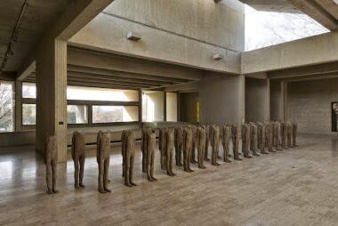 Row of headless sculptures in a concrete room.
