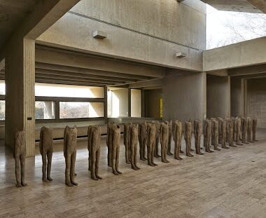 Row of headless sculptures in a concrete room.