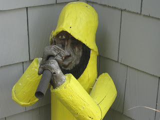 Wooden figure in yellow raincoat holding pipe.