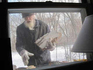 Man outside window holding firewood in winter.