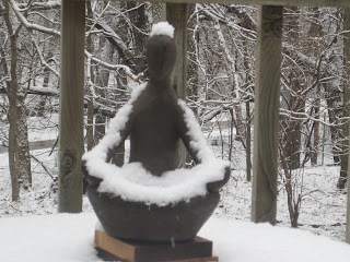 Snow-covered statue in a snowy forest.