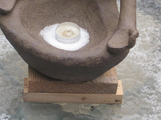 Candle in bowl with snow on pedestal.