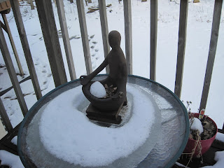 Statue on snowy table by wooden railing.