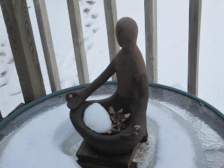 Statue holding snowball on snowy table.