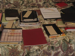 Notebooks and journals spread on floral bedspread.