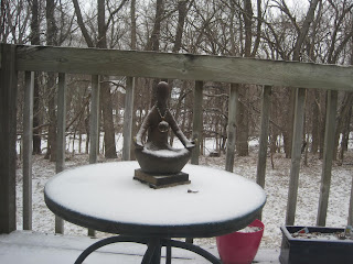 Snow-covered table with small statue outside.