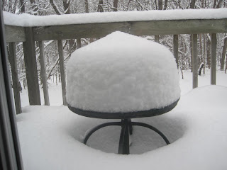 Snow-covered patio table and railing outside window.