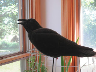 Black crow sculpture near a window indoors.
