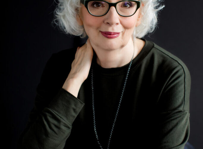 Elderly woman with glasses, white hair, smiling.